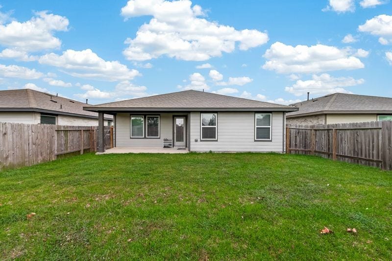 7523 Keystone Blossom Trail, Richmond, TX 77407 Centered rear elevation highlighting symmetrical window placement, covered patio access, and a spacious lawn enclosed by full perimeter fencing.
