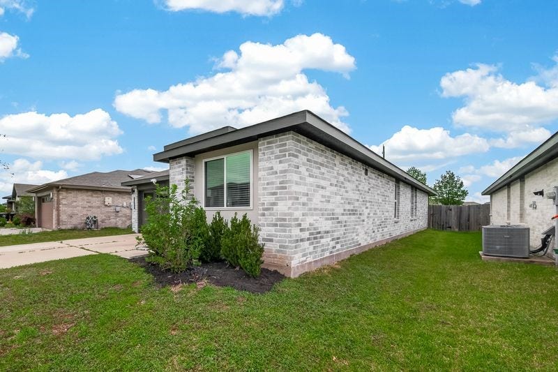 7523 Keystone Blossom Trail, Richmond, TX 77407 Side elevation showcasing the full brick exterior, generous green space, and window placement that allows for natural light along the homes length.