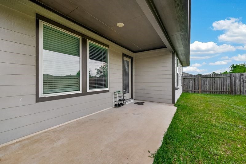 7523 Keystone Blossom Trail, Richmond, TX 77407 Reverse angle of the covered patio highlighting exterior wall finishes, rear windows, and direct access into the home, all overlooking the fenced yard.