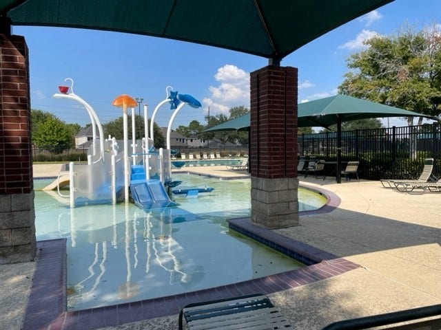 3511 Paigewood Drive, Pearland, TX 77584 Charming community pool area featuring a fun children's splash zone with slides and water features, surrounded by shaded seating for relaxation.