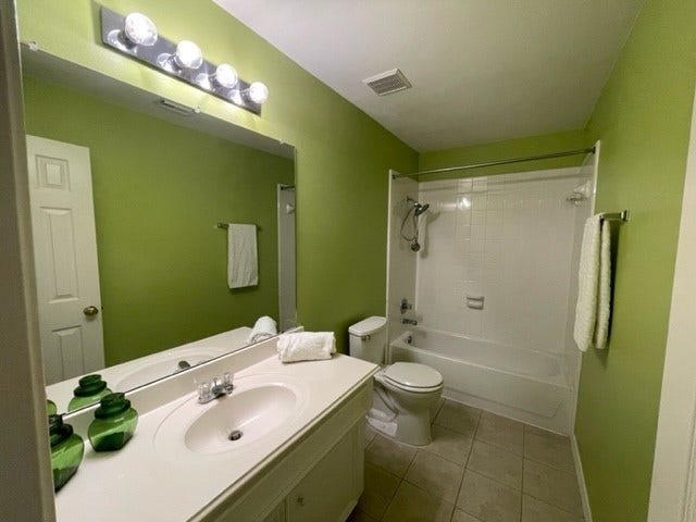 3511 Paigewood Drive, Pearland, TX 77584 Guest bathroom featuring a sleek vanity with sink, a large mirror with modern lighting, and a spacious shower-tub combo, all enhanced by vibrant green walls.