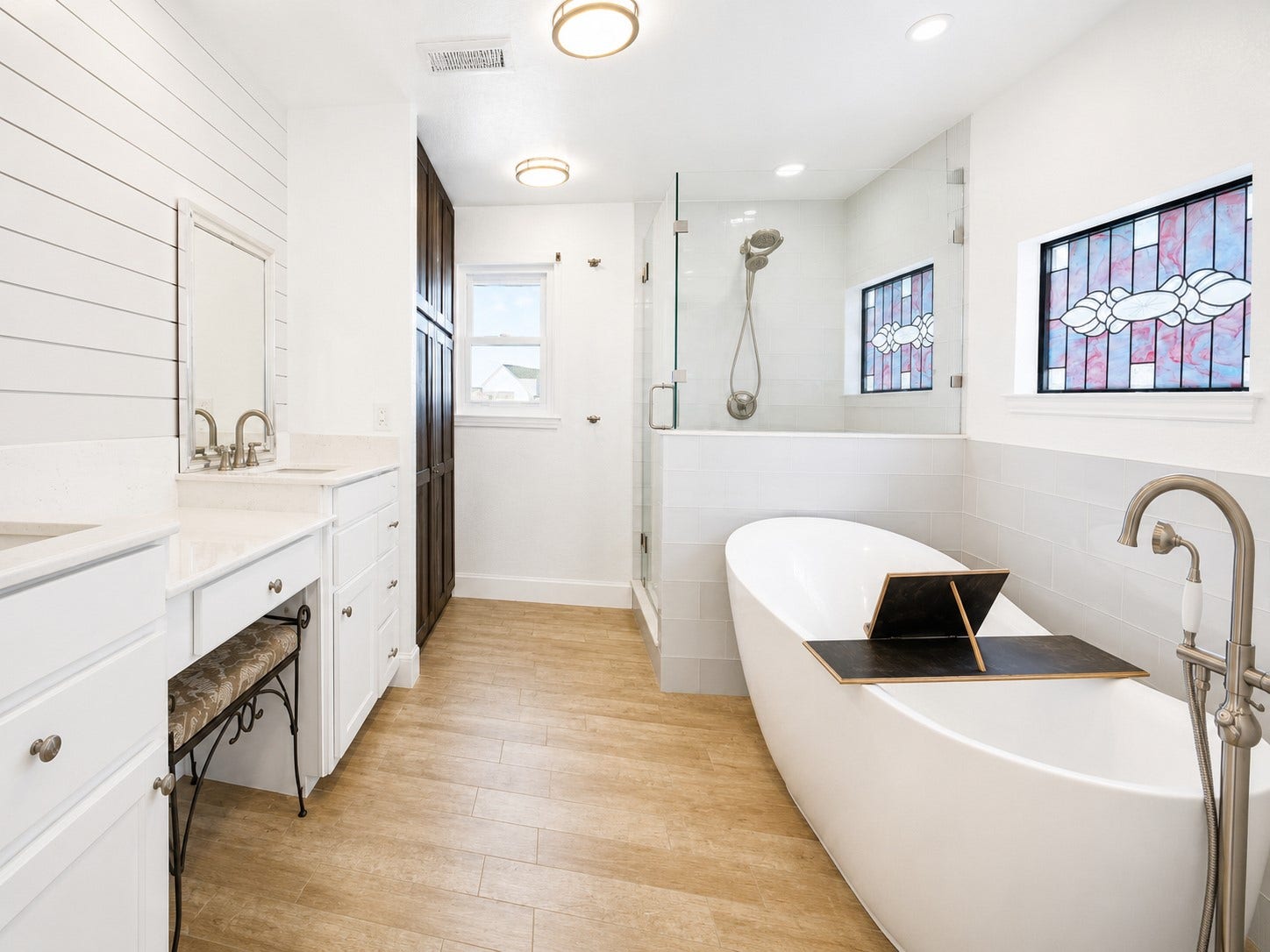 107 Bamaku Bend, Tiki Island, TX 77554 Step into your spa-like primary bath, beautifully updated and designed to easily accommodate two. Individual vanities set against a character-rich shiplap wall, a soaking tub, glass-enclosed shower, dedicated makeup vanity and custom floor-to-ceiling linen cabinet bring function and storage to the room.