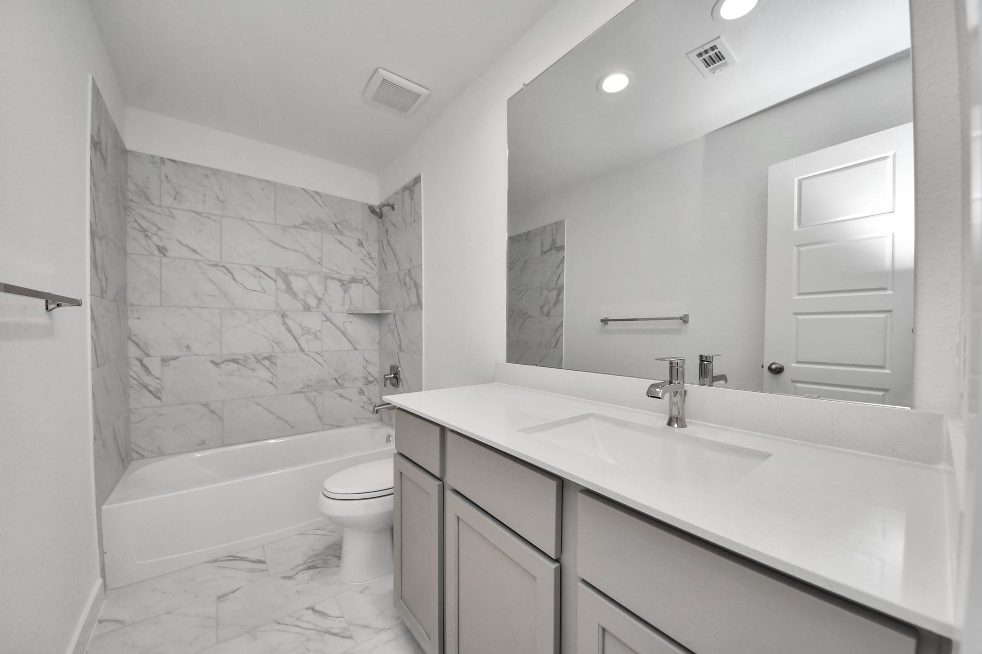Secondary bath features tile flooring, bath/shower combo with tile surround, light stained wood cabinets, beautiful light countertop. Sample photo of completed home with similar floor plan. Actual colors and selections may vary.