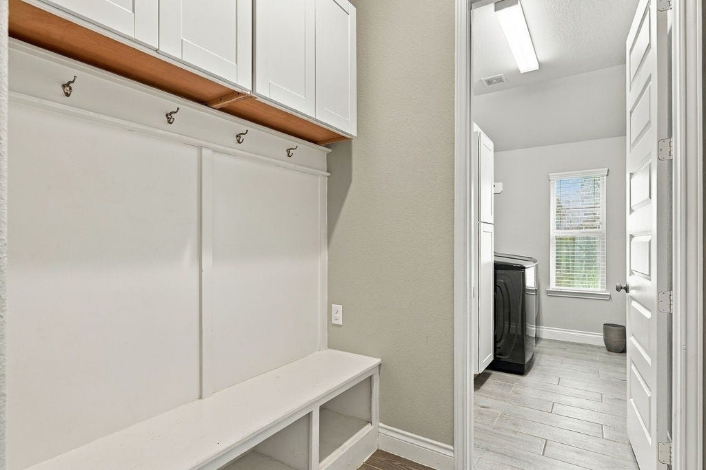 6914 Red Oak Drive, Katy, TX 77493 Spacious mudroom features built-in storage with hooks and a bench, leading into a bright, modern laundry room with ample natural light.