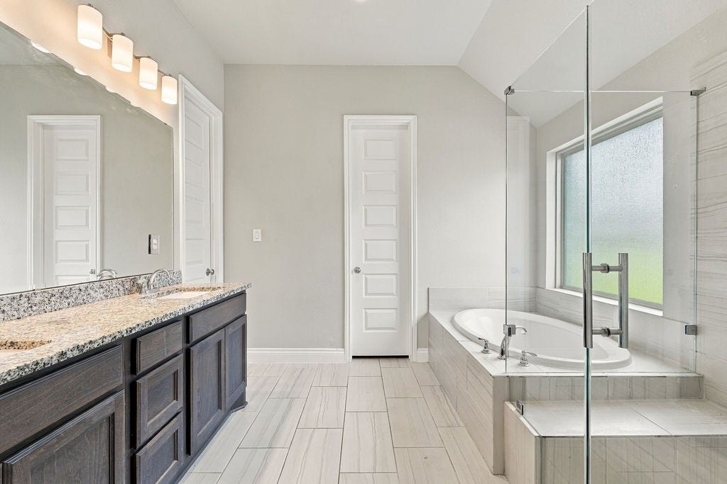 6914 Red Oak Drive, Katy, TX 77493 Elegant bathroom featuring a spacious double vanity with granite countertops, a luxurious soaking tub, and a modern glass-enclosed shower, all accented by sleek tile flooring and ample natural light.
