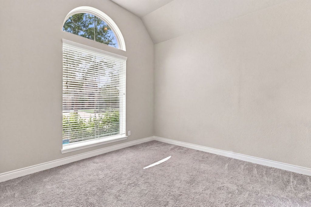 6914 Red Oak Drive, Katy, TX 77493 Bright room with a large arched window, plush carpet, and neutral walls, perfect for a cozy retreat or home office.