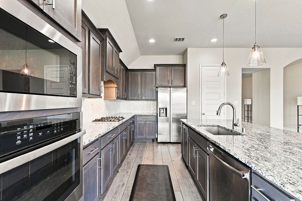 6914 Red Oak Drive, Katy, TX 77493 Stunning modern kitchen featuring sleek stainless steel appliances, elegant dark cabinetry, and a spacious granite island with pendant lighting, perfect for culinary enthusiasts.