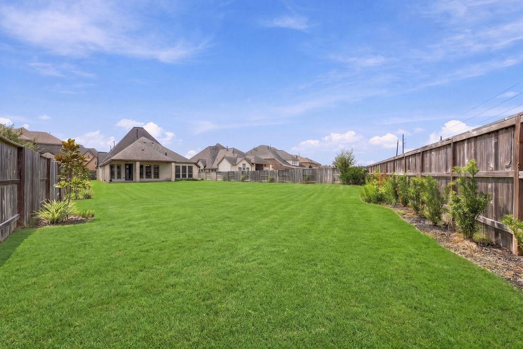 6914 Red Oak Drive, Katy, TX 77493 Expansive backyard with lush green lawn, bordered by a wooden fence and landscaping, perfect for outdoor activities and privacy.