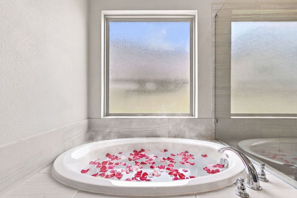 6914 Red Oak Drive, Katy, TX 77493 Indulge in relaxation with a luxurious soaking tub, enhanced by frosted windows for privacy and adorned with delicate rose petals.