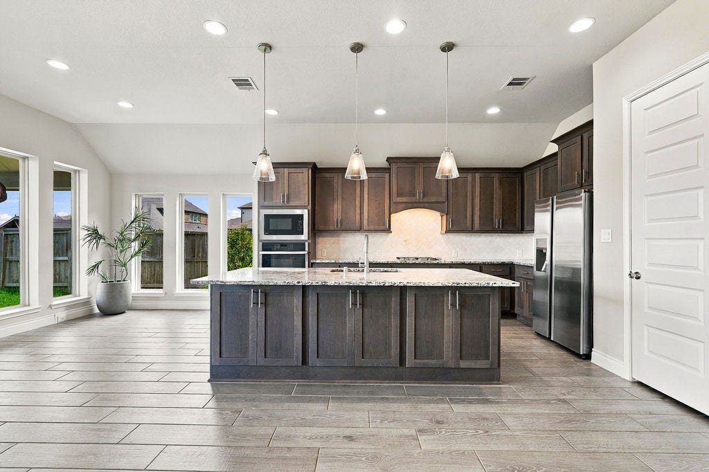 6914 Red Oak Drive, Katy, TX 77493 Spacious kitchen with elegant dark wood cabinetry, a large central island, and modern stainless steel appliances, complemented by abundant natural light streaming through expansive windows.