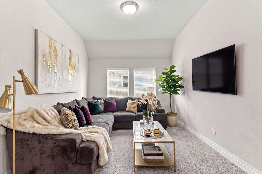 6914 Red Oak Drive, Katy, TX 77493 Cozy living room with a plush sectional sofa adorned with colorful cushions, complemented by a modern coffee table and a large wall-mounted TV for entertainment.