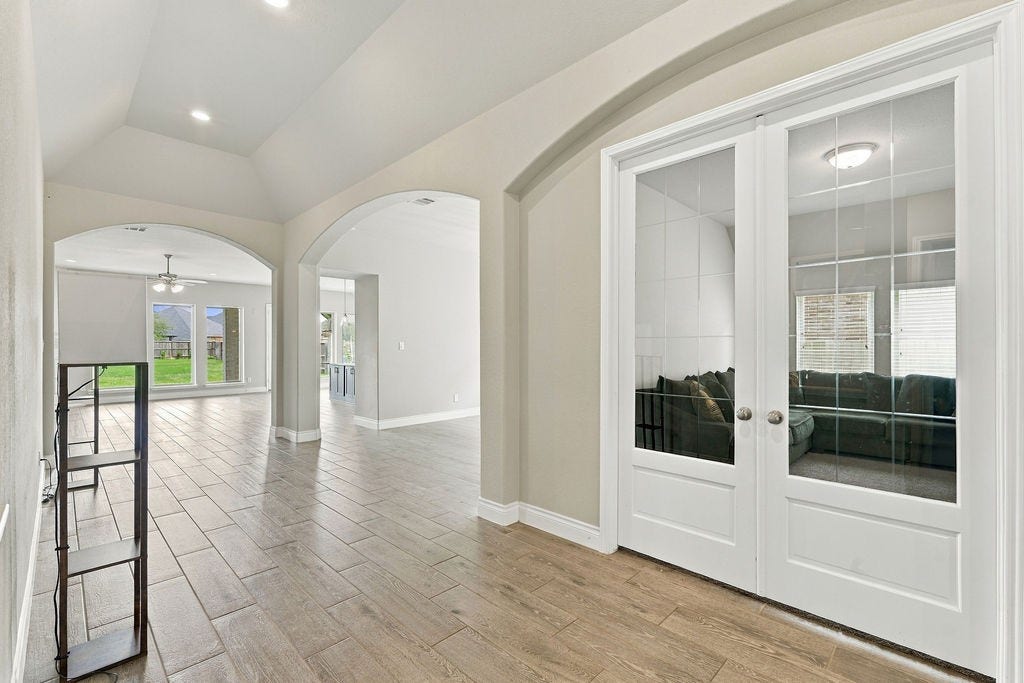 6914 Red Oak Drive, Katy, TX 77493 Elegant entryway with arched doorways leads to a spacious living area. Beautiful wood-look flooring and French doors enhance the open, airy feel.