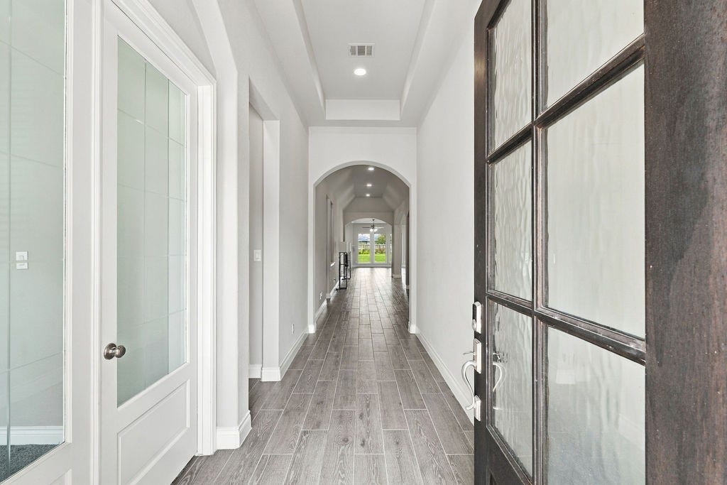6914 Red Oak Drive, Katy, TX 77493 Step into a bright and inviting entryway featuring elegant wood-look tile flooring, high ceilings, and a long hallway that leads to spacious living areas filled with natural light.