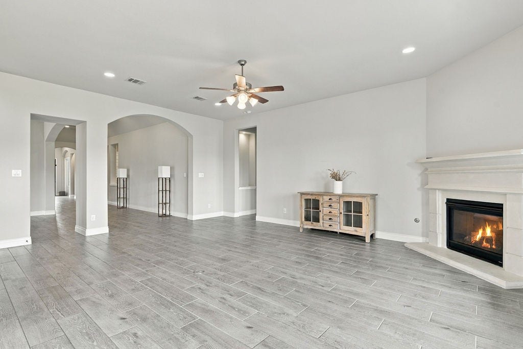 6914 Red Oak Drive, Katy, TX 77493 Spacious living room featuring elegant gray hardwood floors, a cozy fireplace, and stylish archways complemented by soft lighting and a ceiling fan.