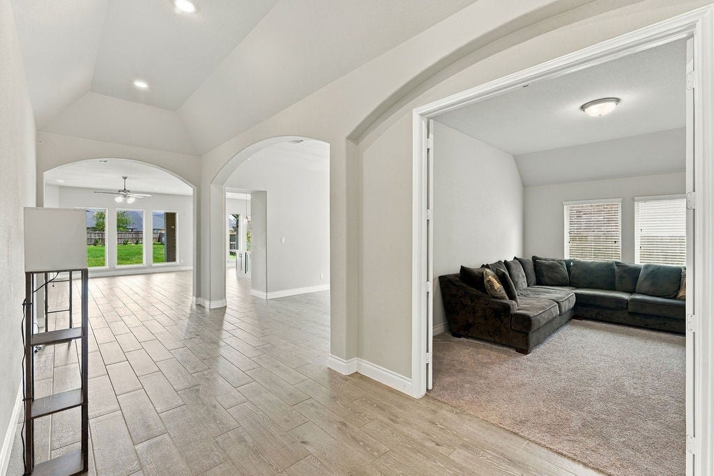 6914 Red Oak Drive, Katy, TX 77493 Experience open-concept living with this spacious hallway featuring elegant archways, a cozy carpeted sitting room, and abundant natural light from large windows overlooking the green backyard.