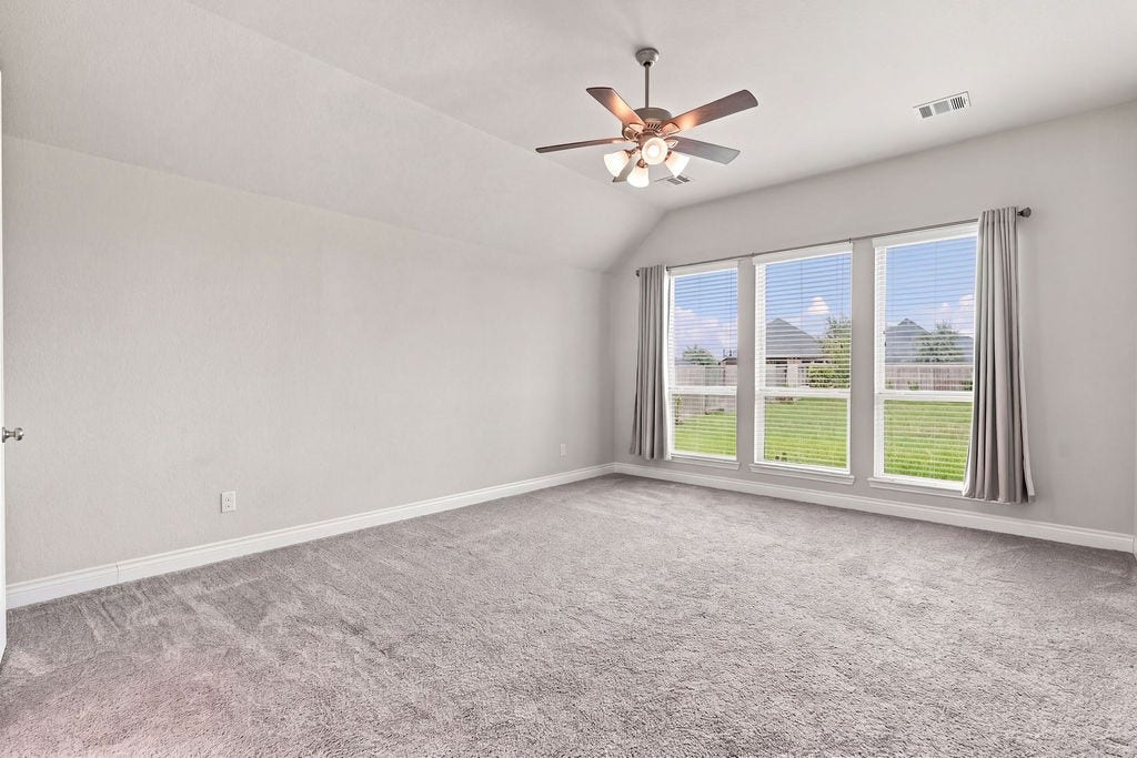 6914 Red Oak Drive, Katy, TX 77493 Spacious, light-filled bedroom with plush carpeting, large windows offering serene backyard views, and a ceiling fan for comfort.