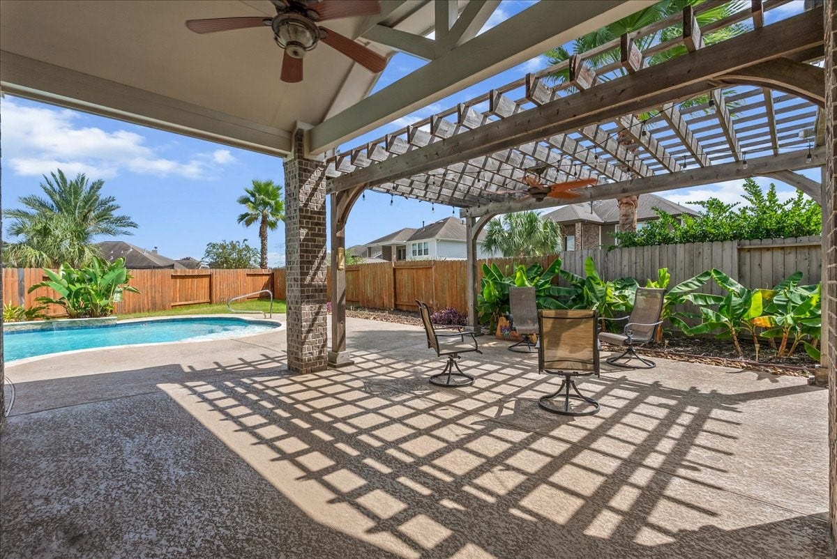 Imagine your family enjoying outdoor living with a spacious patio featuring a pergola, ceiling fan, and stylish seating area, overlooking a sparkling pool surrounded by lush greenery.