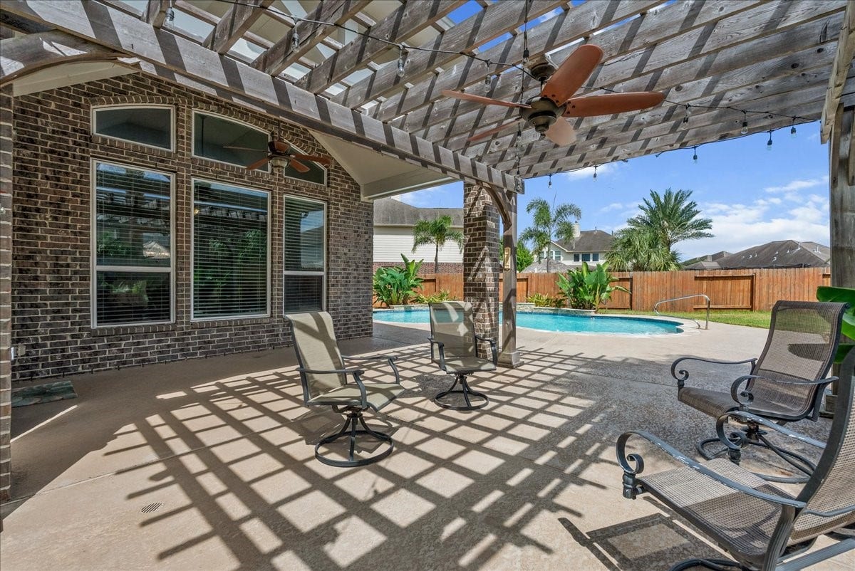 Relax in a spacious backyard oasis featuring a covered patio with ceiling fans, perfect for entertaining, overlooking a sparkling pool and lush landscaping.