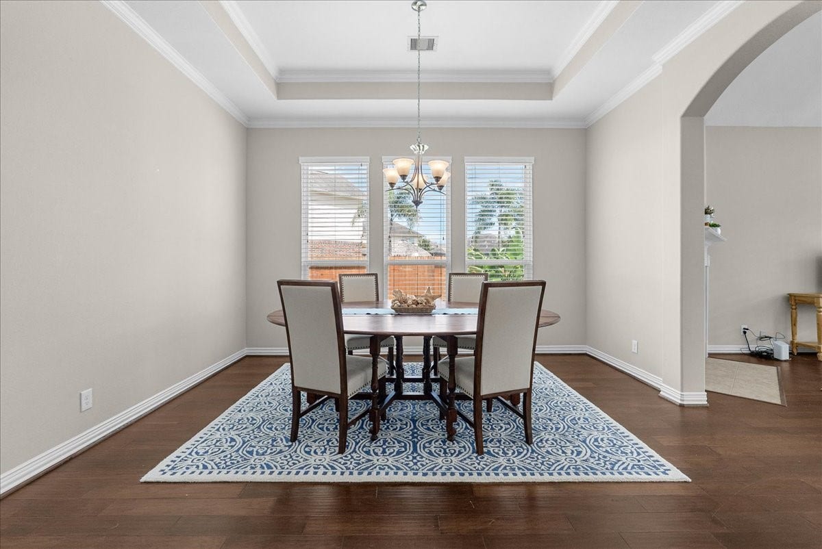 One more photo of the spacious dining room with a tray ceiling, featuring a stylish chandelier and large windows that offer plenty of natural light, complemented by classic engineered wood floors