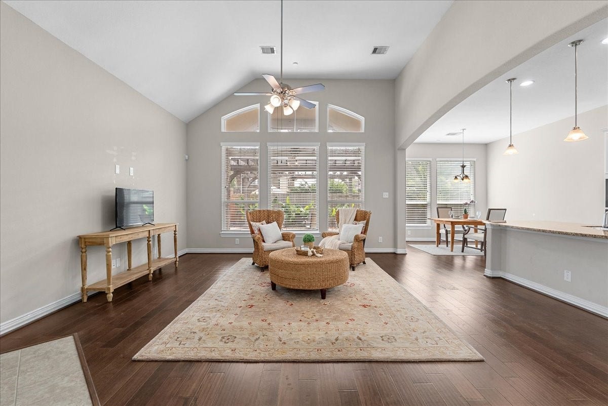 Spacious living area with high ceilings, abundant natural light, and elegant engineered hardwood floors. The open layout seamlessly connects to a cozy dining space and a modern kitchen with stylish pendant lighting.