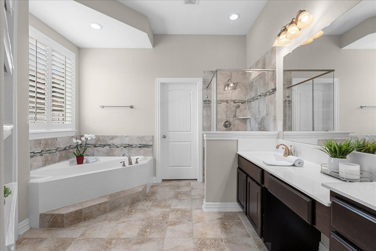 Come enjoy this luxurious bathroom featuring a spacious soaking tub, elegant dual vanities, and a sleek glass-enclosed shower, all accentuated by soft, neutral tones and ample natural light.