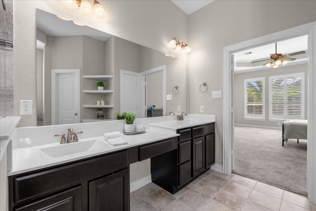 Spacious bathroom with dual sinks, elegant fixtures, and ample storage, seamlessly connecting to a bright bedroom featuring large windows that overlook the backyard area.