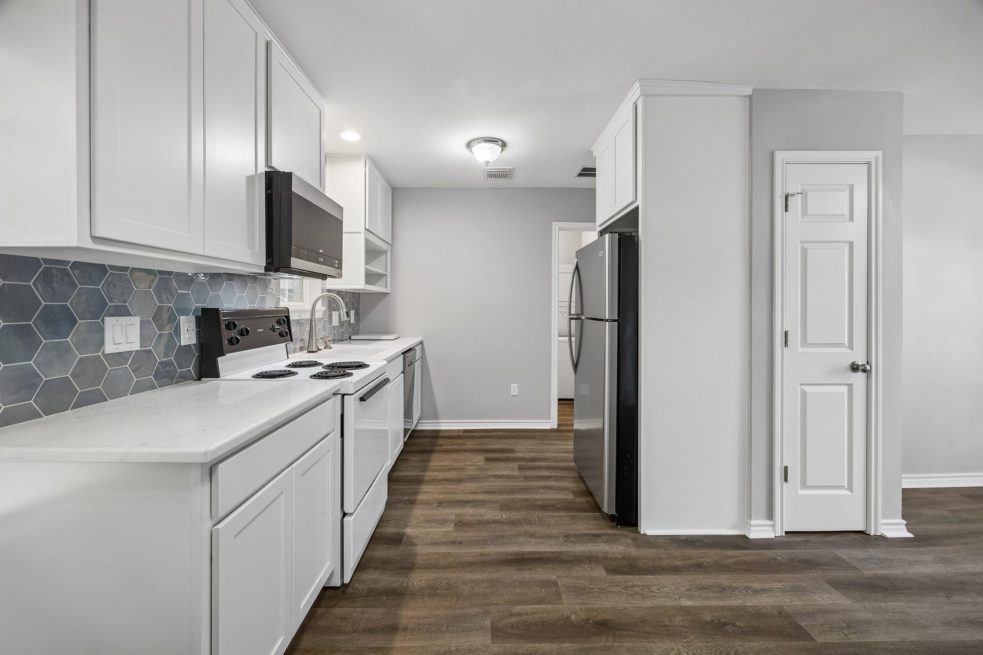 1439 Waverly Street, Houston, TX 77008 Garage apartment kitchen with white cabinetry, stainless steel appliances, and engineered wood flooring, offering a functional, well-appointed space for guests or extended stays.