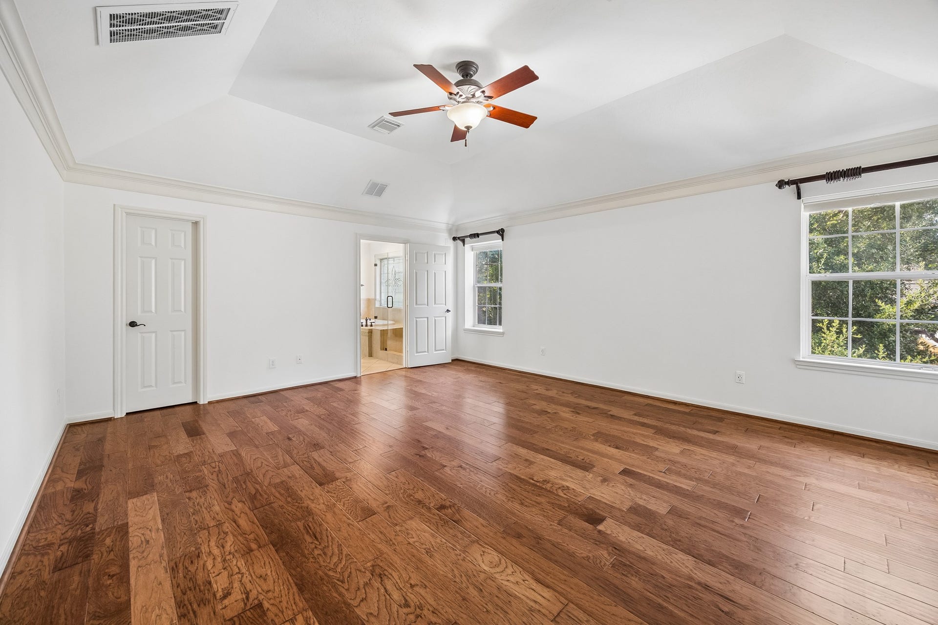 1439 Waverly Street, Houston, TX 77008 Spacious primary bedroom with rich hardwood floors, custom window treatments, and a ceiling fan, creating a comfortable and inviting retreat.