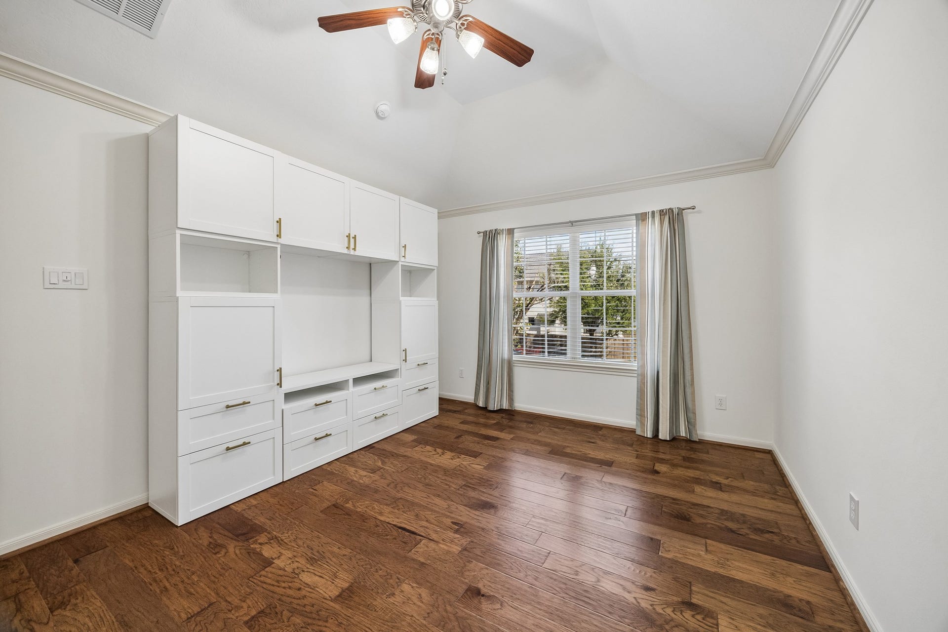 1439 Waverly Street, Houston, TX 77008 Secondary bedroom with hardwood floors, custom built-in shelving and cabinetry, and a ceiling fan, offering excellent storage and flexibility.