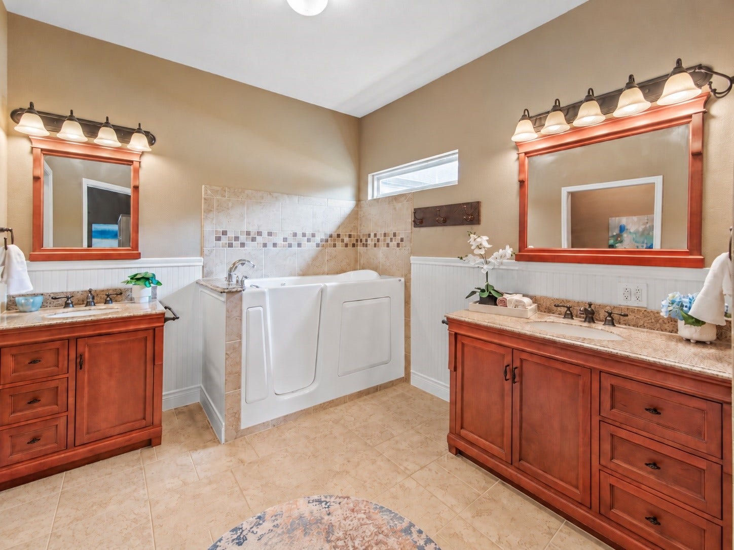 16144 Firetower Road, Conroe, TX 77306 Primary bath featuring two separate vanities with generous storage, a walk-in tub, and decorative tile accents complemented by beadboard wainscoting.