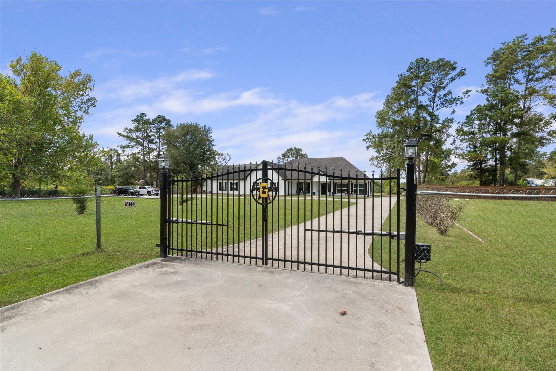 16144 Firetower Road, Conroe, TX 77306 Decorative automatic entry gate with lantern-topped posts creates a welcoming entrance, with a long concrete driveway leading to the home.