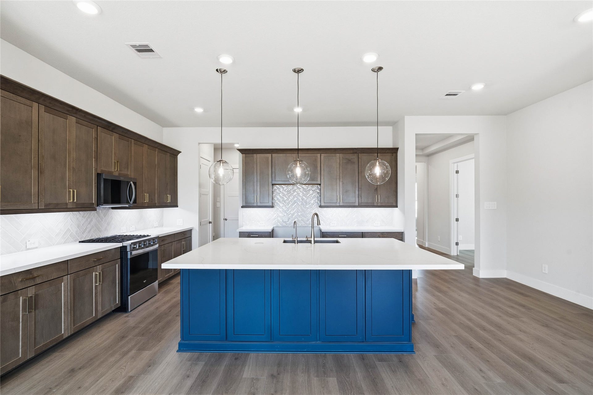 The kitchen anchors the space with warm, dark wood cabinetry, stainless steel appliances, sleek white quartz countertops, and a large island perfect for casual dining or hosting.