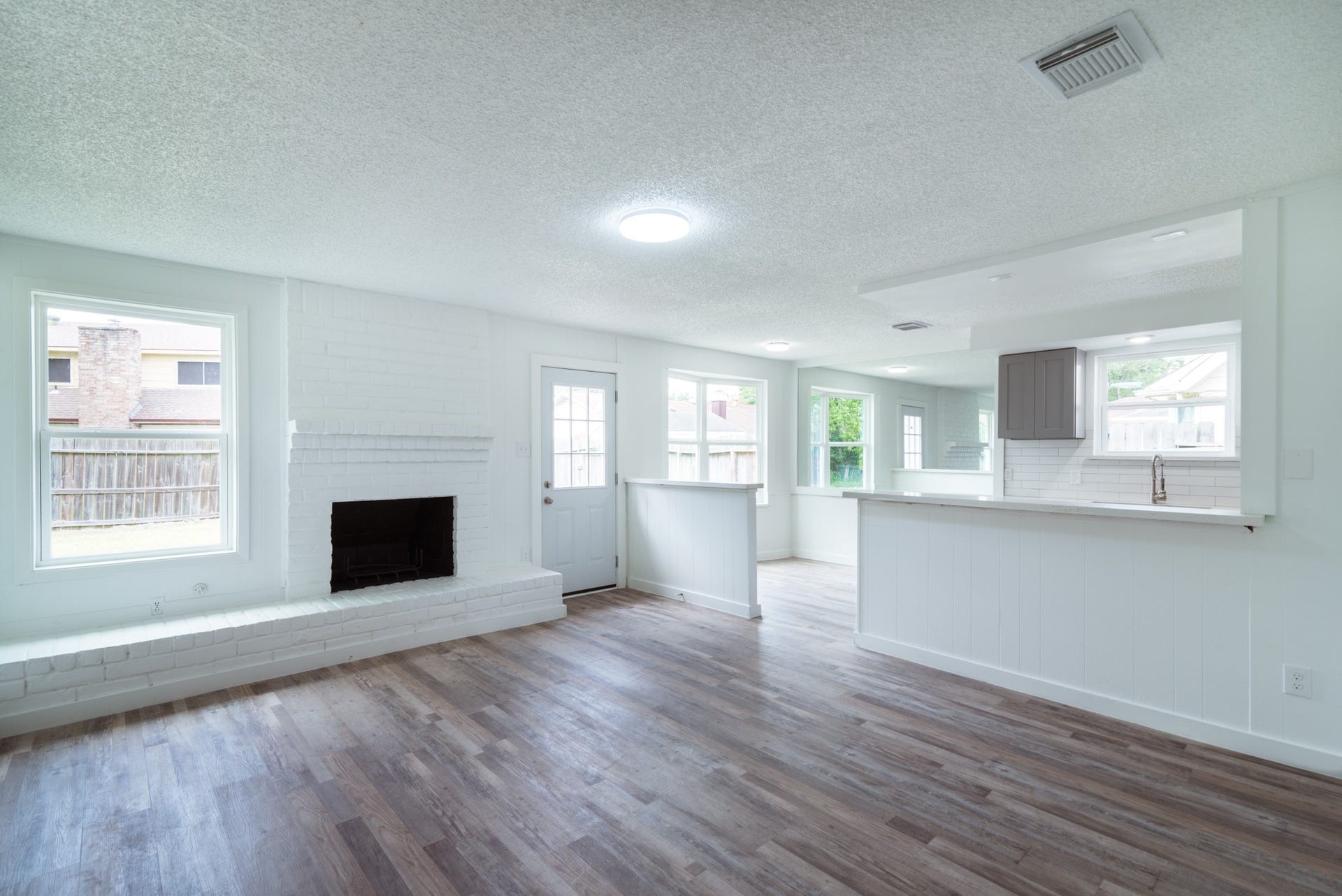 15910 Plagens Lane, Missouri City, TX 77489 Bright and airy living space featuring a cozy white brick fireplace, open layout, and abundant natural light from large windows. The adjacent kitchen offers a sleek design with modern finishes.