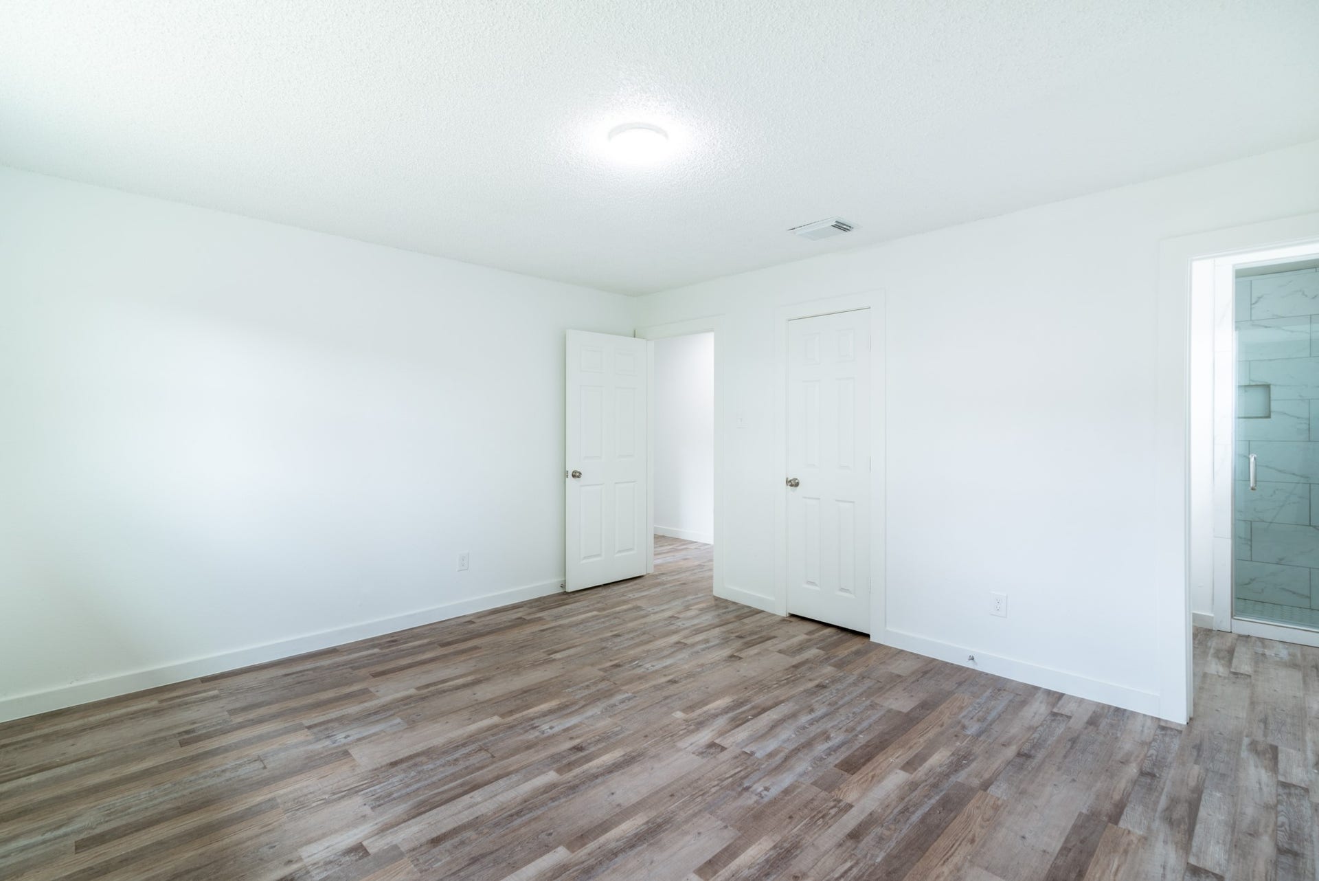 15910 Plagens Lane, Missouri City, TX 77489 Bright and airy bedroom featuring sleek wood-look flooring, fresh white walls, and convenient access to a modern en-suite bathroom.