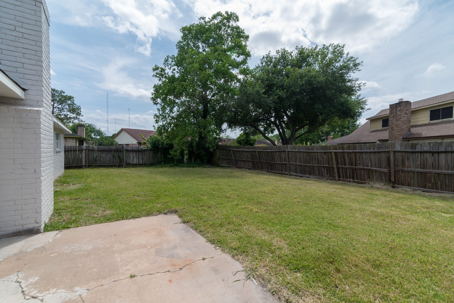 15910 Plagens Lane, Missouri City, TX 77489 Spacious backyard featuring a lush lawn and mature trees, perfect for outdoor activities and relaxation, enclosed by a rustic wooden fence for privacy.
