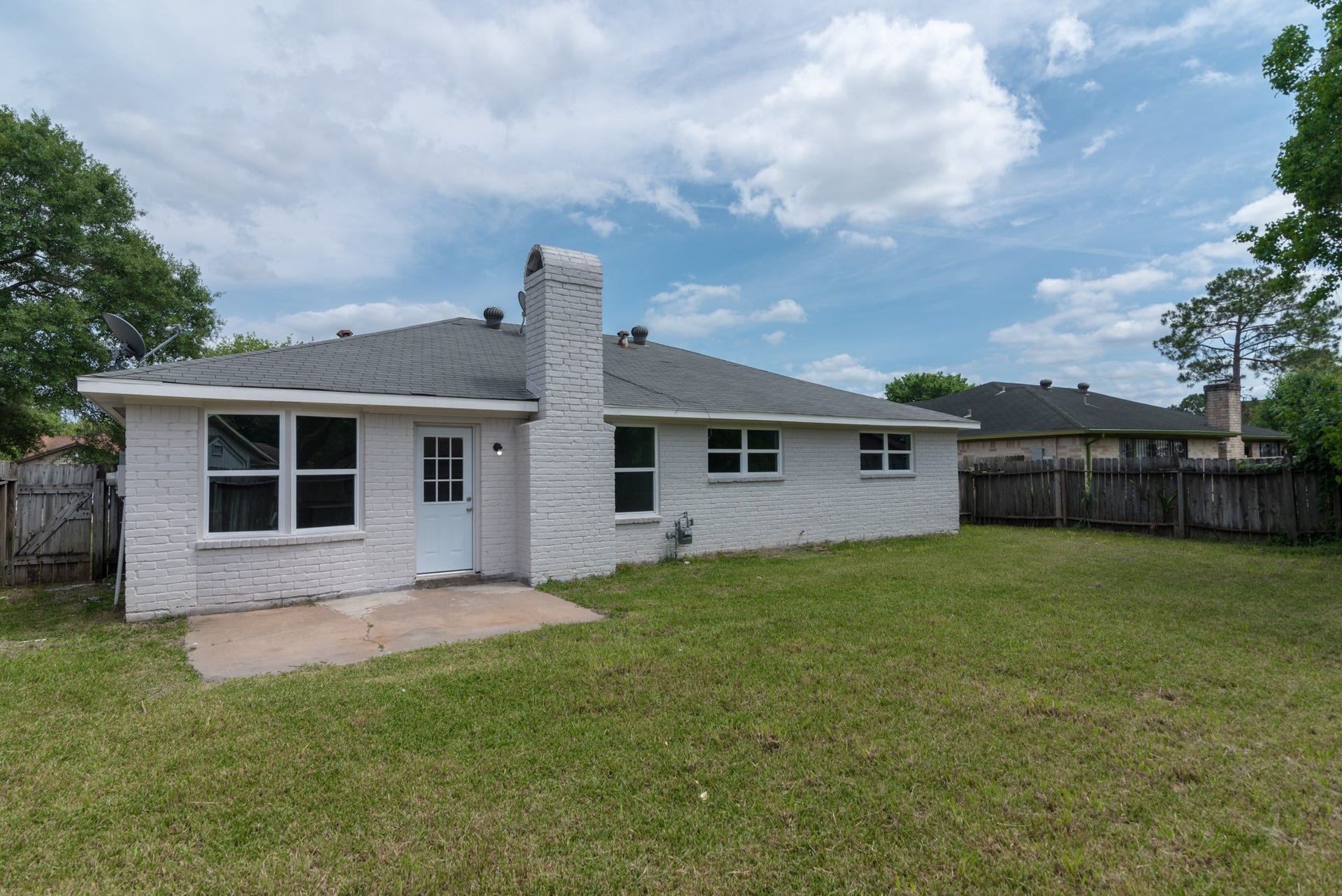 15910 Plagens Lane, Missouri City, TX 77489 Charming single-story home with a spacious backyard, featuring a white brick exterior, inviting patio area, and ample green space for outdoor activities.