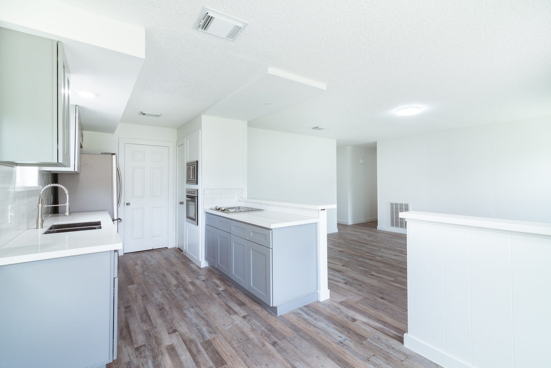 15910 Plagens Lane, Missouri City, TX 77489 Bright and airy kitchen featuring sleek grey cabinetry, modern stainless steel appliances, and elegant wood flooring, seamlessly flowing into the open living area.