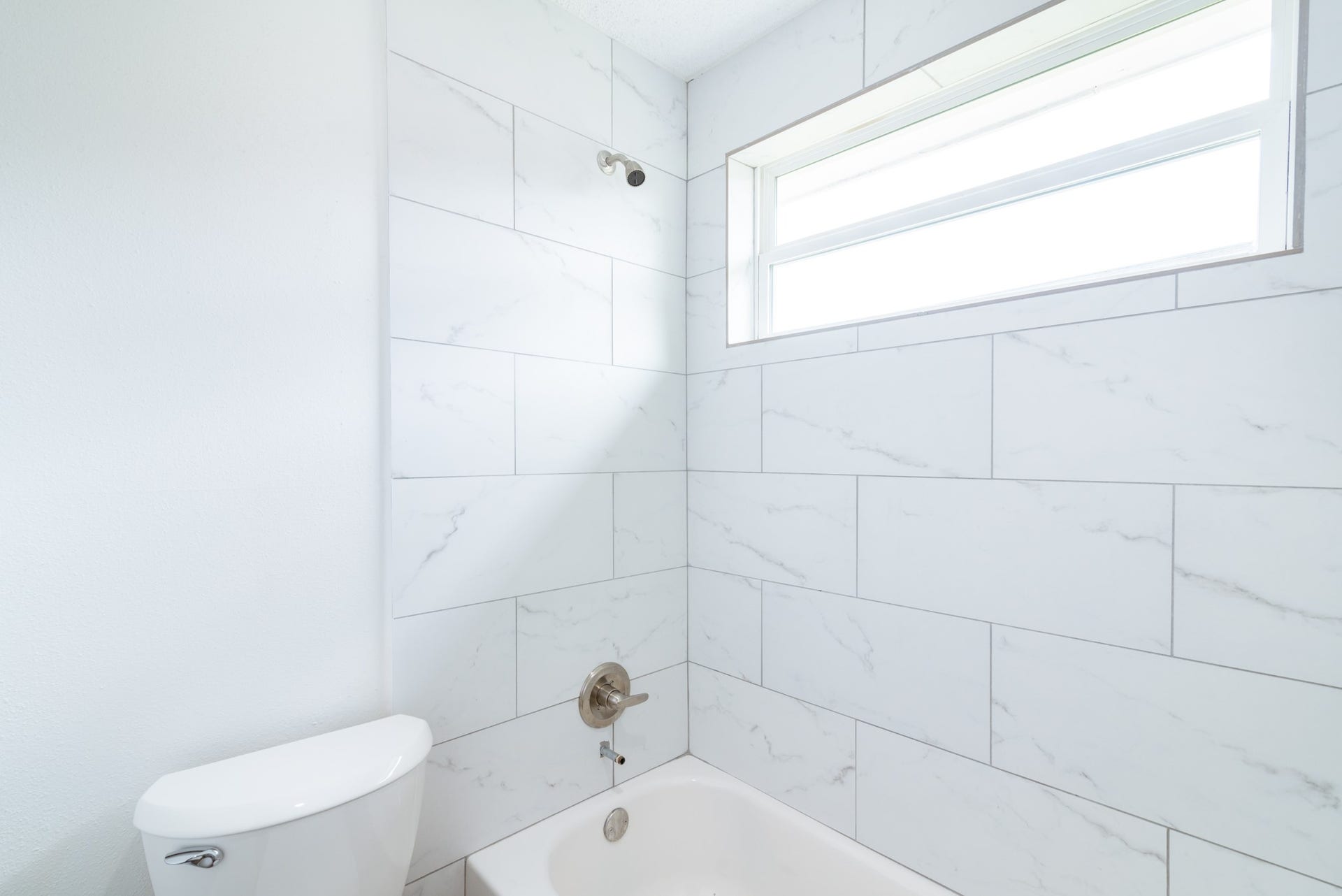 15910 Plagens Lane, Missouri City, TX 77489 Bright and modern bathroom featuring elegant white tile with subtle veining, complemented by a sleek window that invites natural light.