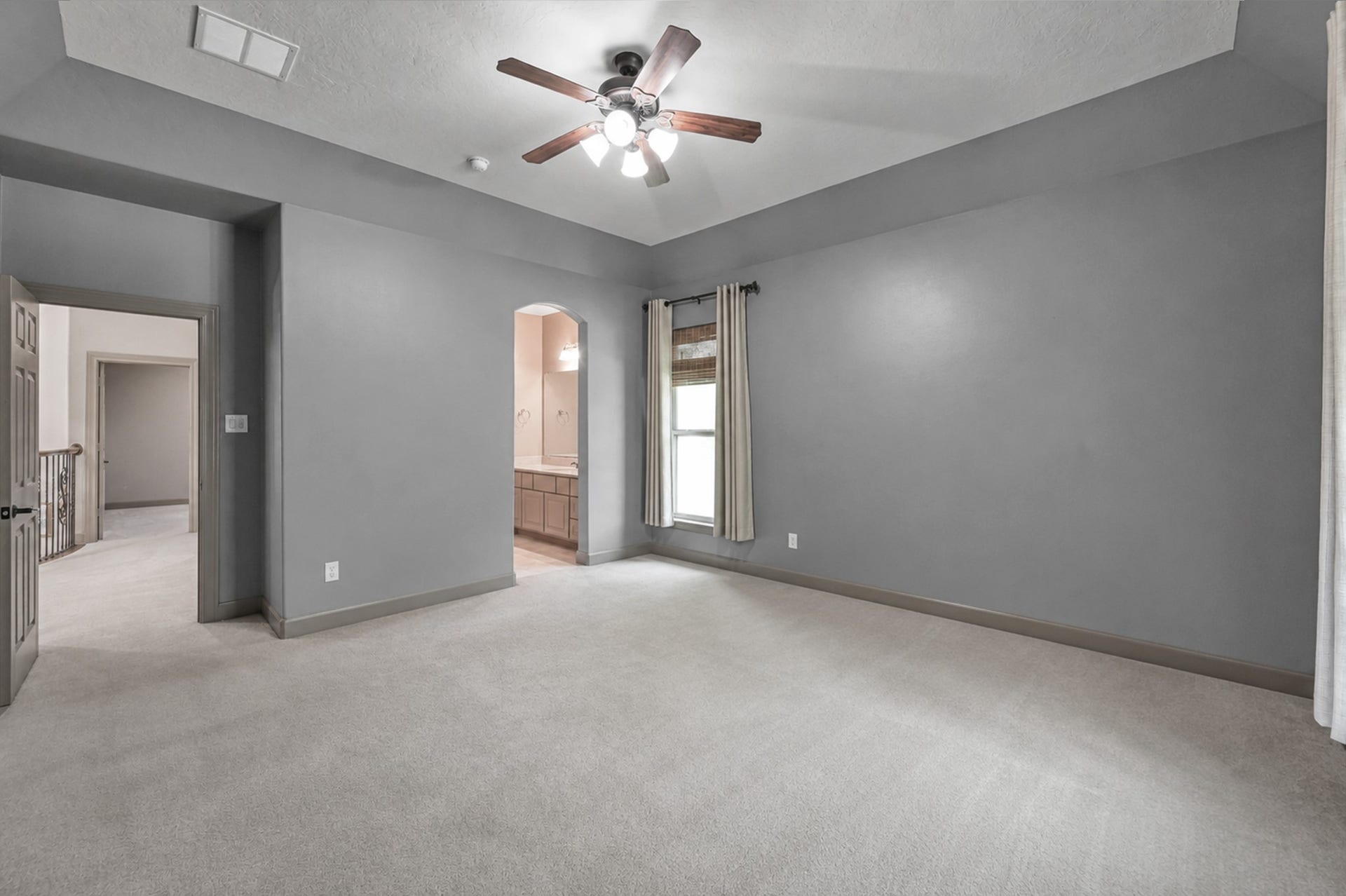 Secondary upstairs bedroom with high vaulted ceiling, central fan, and direct archway access to its dedicated vanity space in the connected Jack-and-Jill bath.
