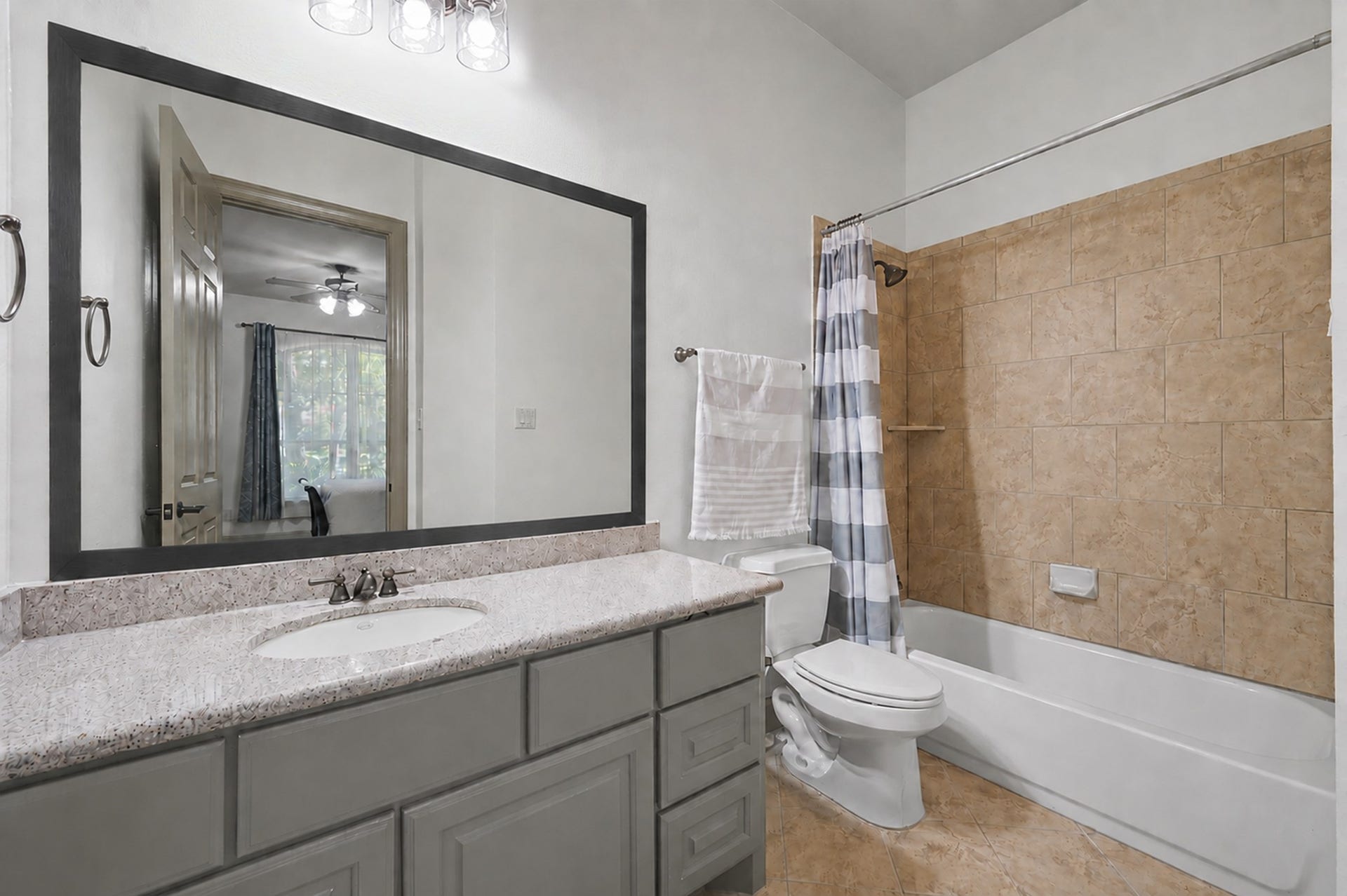 Private ensuite bathroom with granite vanity top, painted cabinets, tile flooring, and a tub/shower combo with tile surround.