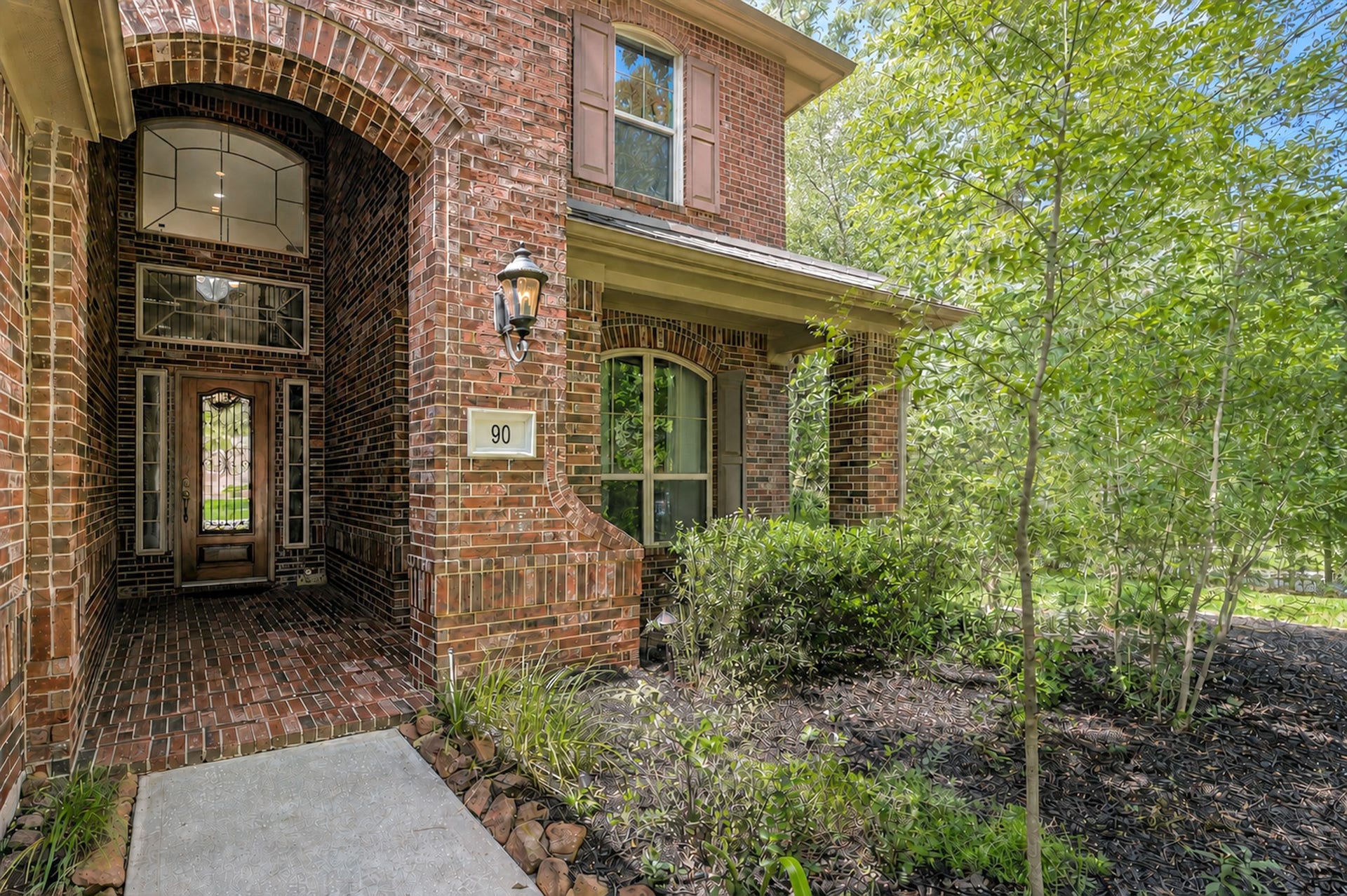 Welcoming entrance with an arched doorway and decorative porch lighting, offering a inviting path to the front door.