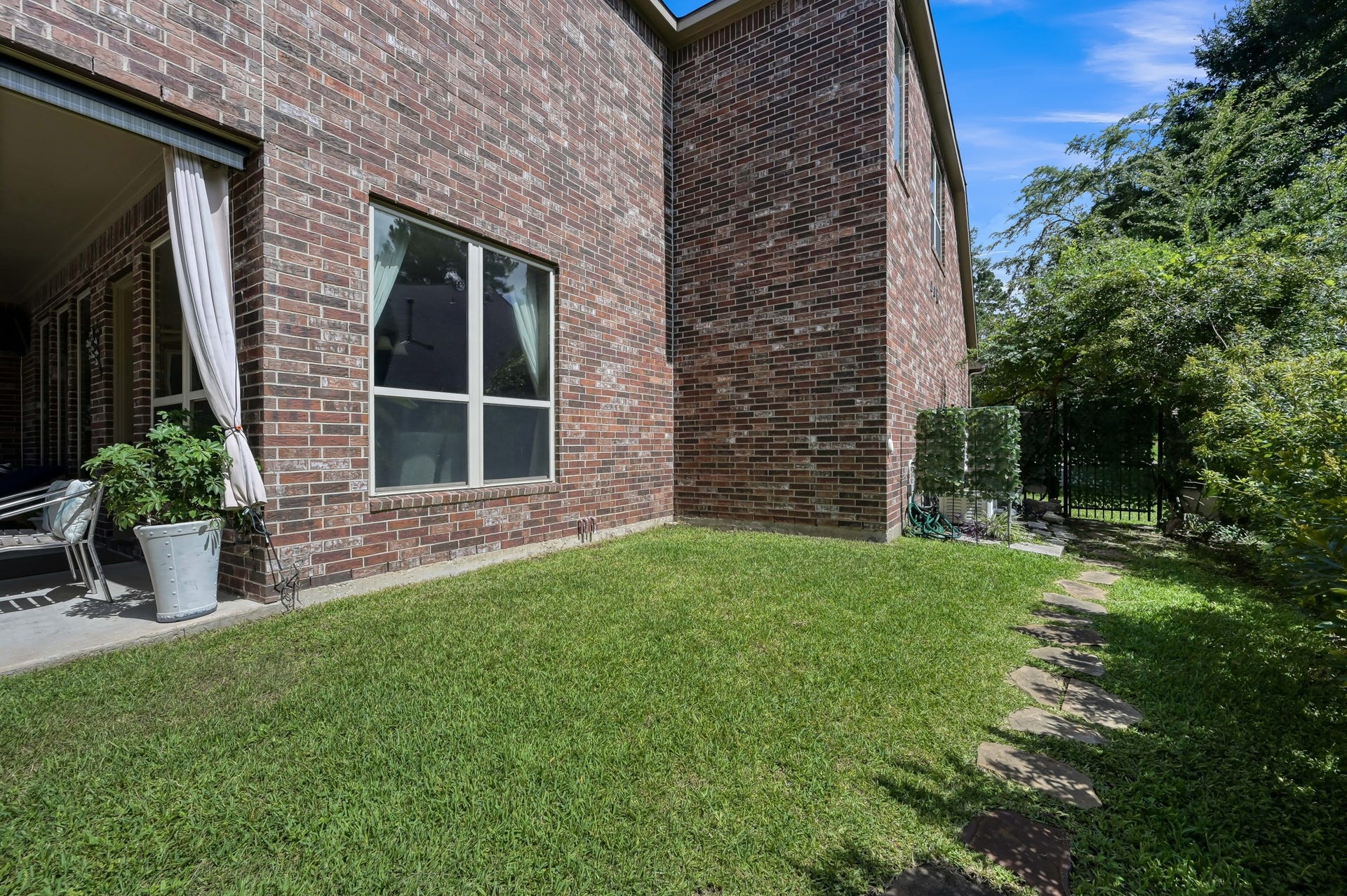 Clean side yard featuring a lush, green lawn section, stepping stone walkway, gated perimeter access, and direct access right off the main covered back patio.
