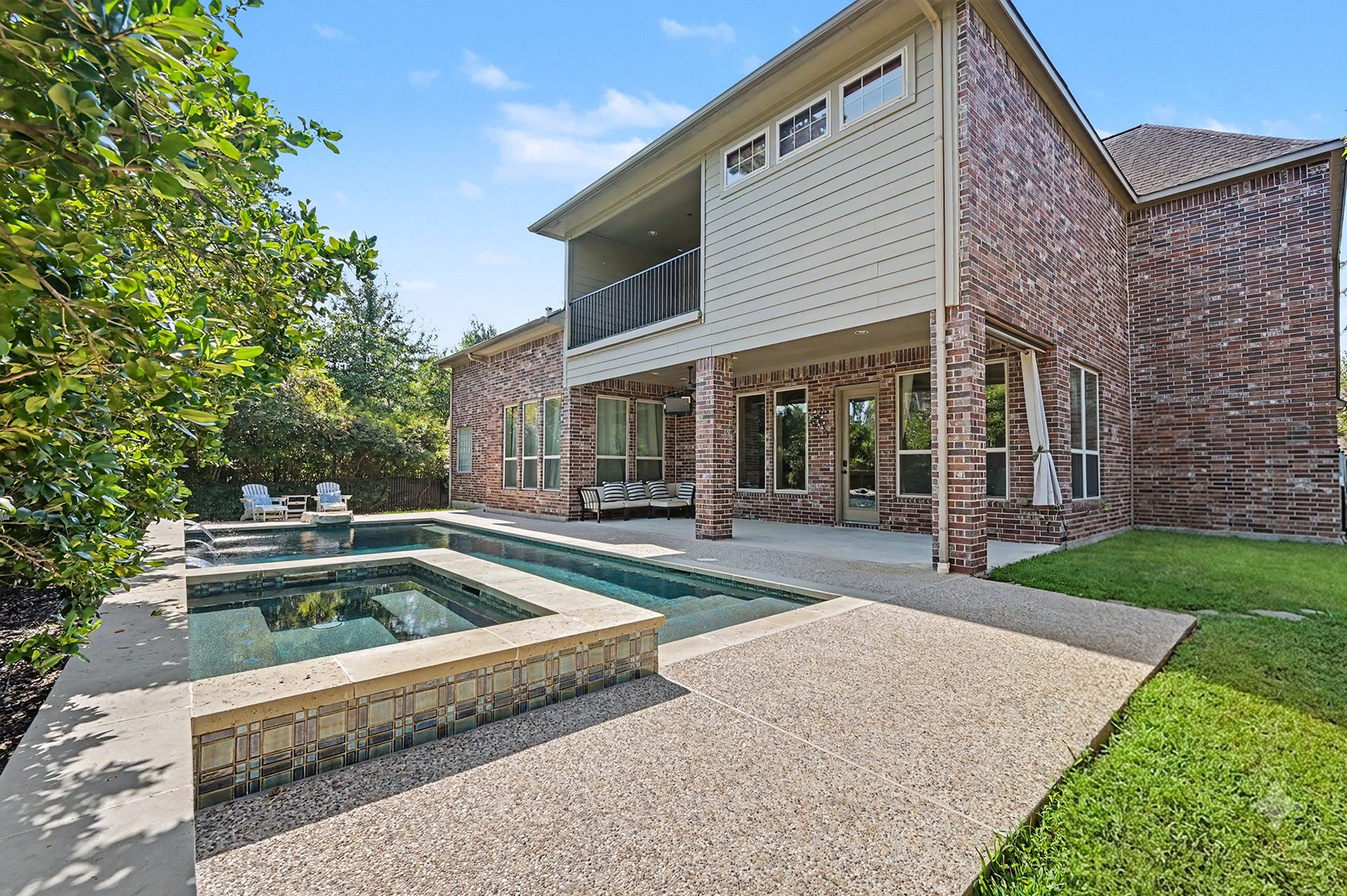Spectacular backyard setup showcasing a sparkling pool with attached spa, large covered patio, and second-story balcony. Complete with low-maintenance decking and a lush patch of usable green grass along the side yard.