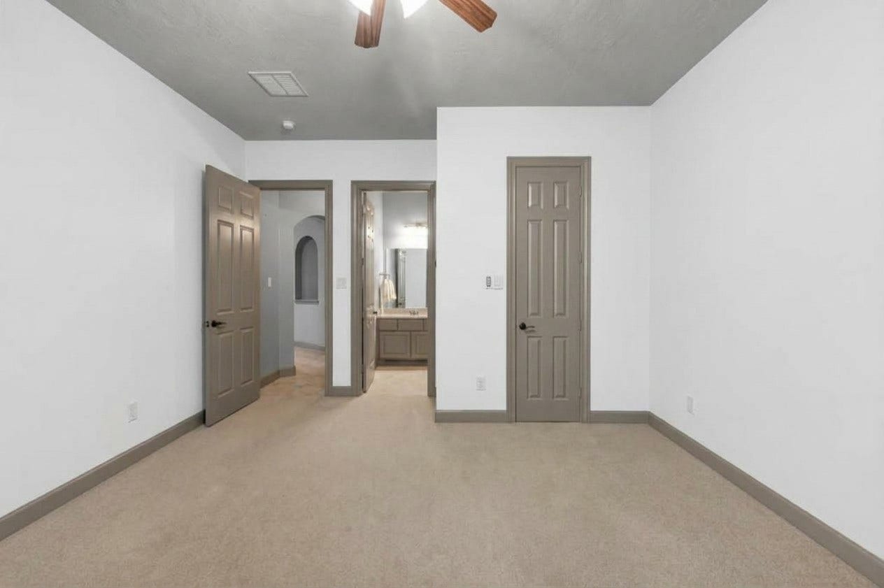 Second downstairs guest bedroom showcasing its dedicated ensuite bath and functional layout. Complete with neutral carpeting, two-tone painted walls, and ceiling fan.