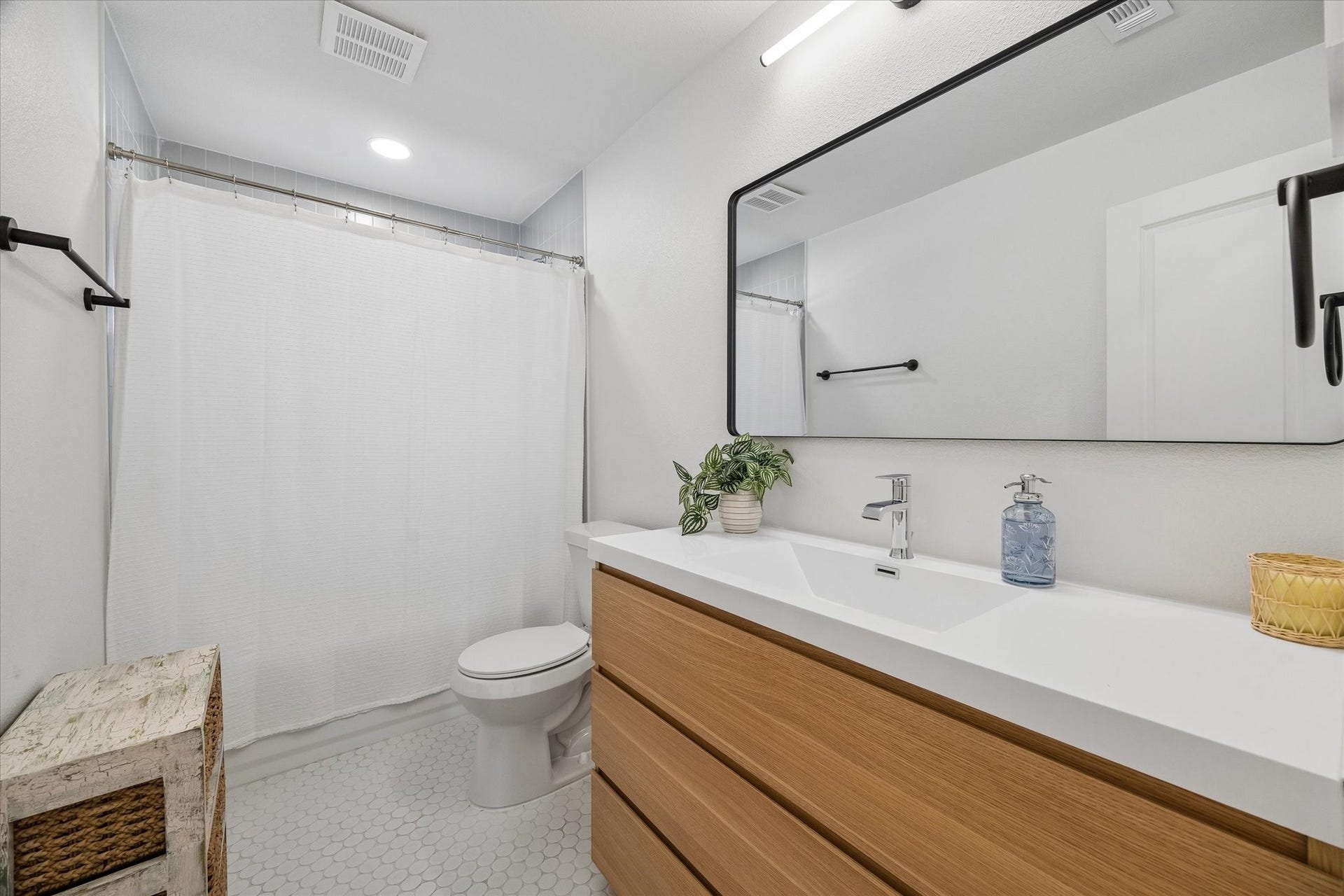 2018 Libbey Drive, Houston, TX 77018 Clean lines give the hall bath a fresh, modern feel, pairing a warm wood vanity with a sleek integrated sink, oversized mirror and classic penny tile flooring.