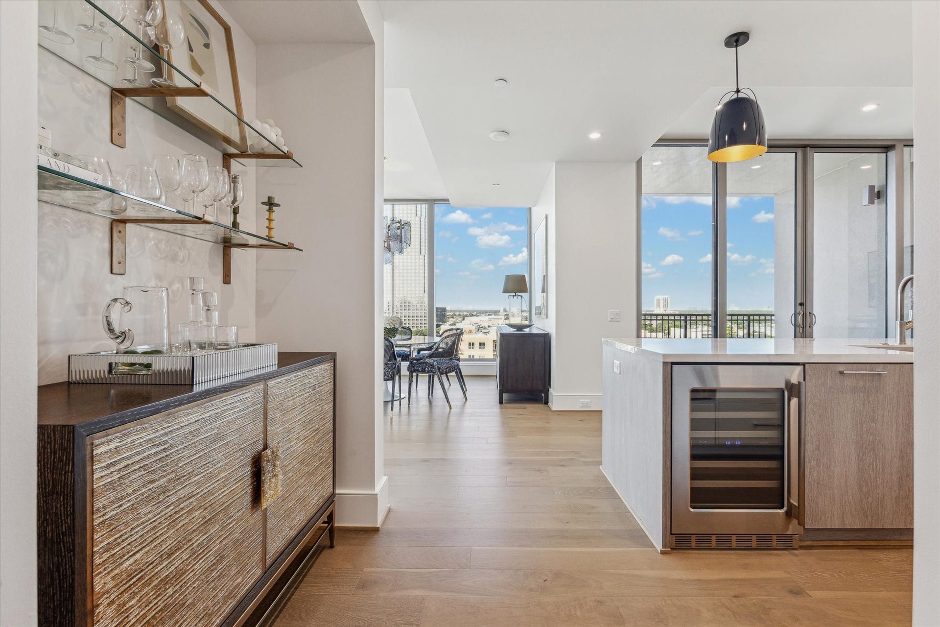 5656 San Felipe Street, #1005, Houston, TX 77056 Entry corridor with glass shelving and an option for a built-in bar, flowing into the open dining and living space framed by large windows and abundant natural light. Photos are of a similar unit with the same floor plan