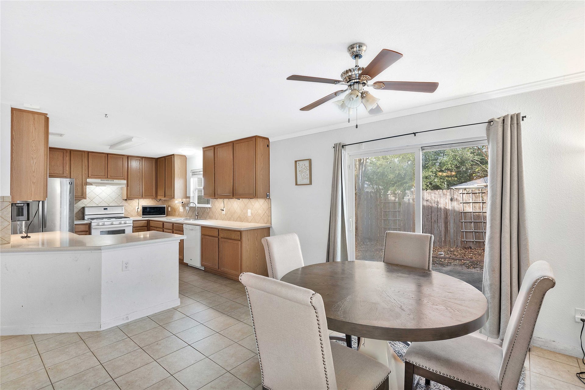 2910 Ribbon Creek Way, Spring, TX 77389 Bright and inviting kitchen and dining area featuring elegant wood cabinetry, modern stainless steel appliances, and a cozy dining space with a view of the backyard through sliding glass doors.