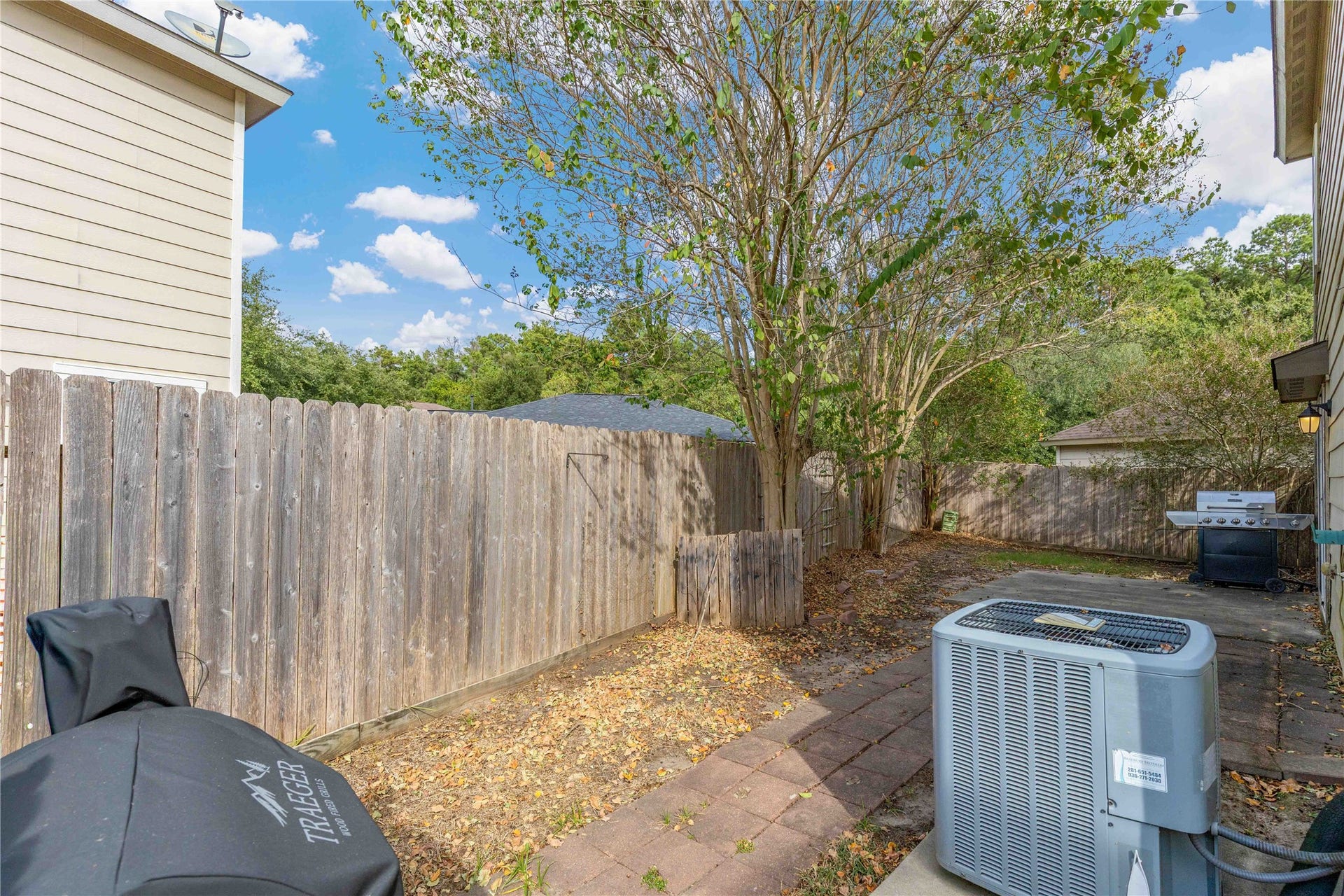 2910 Ribbon Creek Way, Spring, TX 77389 Charming backyard space featuring mature trees, a privacy fence, and a patio area perfect for outdoor grilling and relaxation.