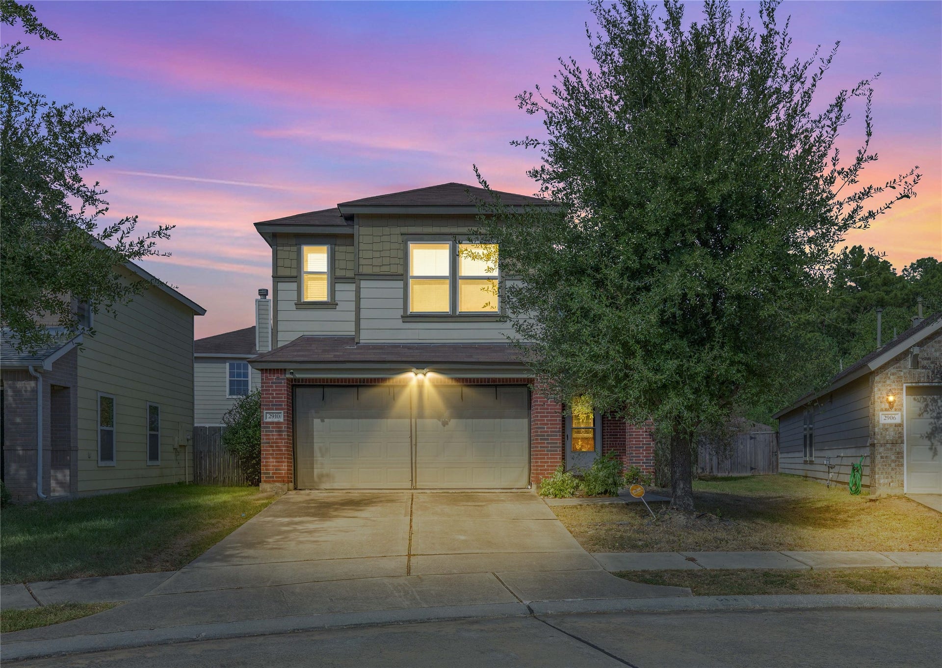 2910 Ribbon Creek Way, Spring, TX 77389 Charming two-story home with a spacious driveway, illuminated at dusk, surrounded by mature trees and featuring a welcoming facade.