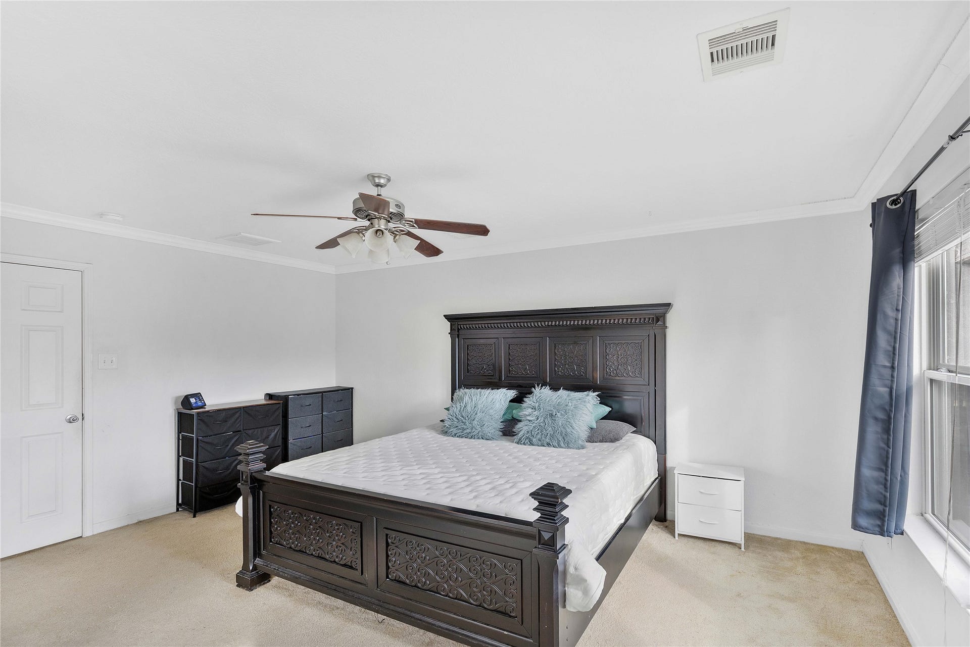 2910 Ribbon Creek Way, Spring, TX 77389 Spacious bedroom featuring a classic dark wood bed frame, carpeted flooring, and ample natural light from large windows.